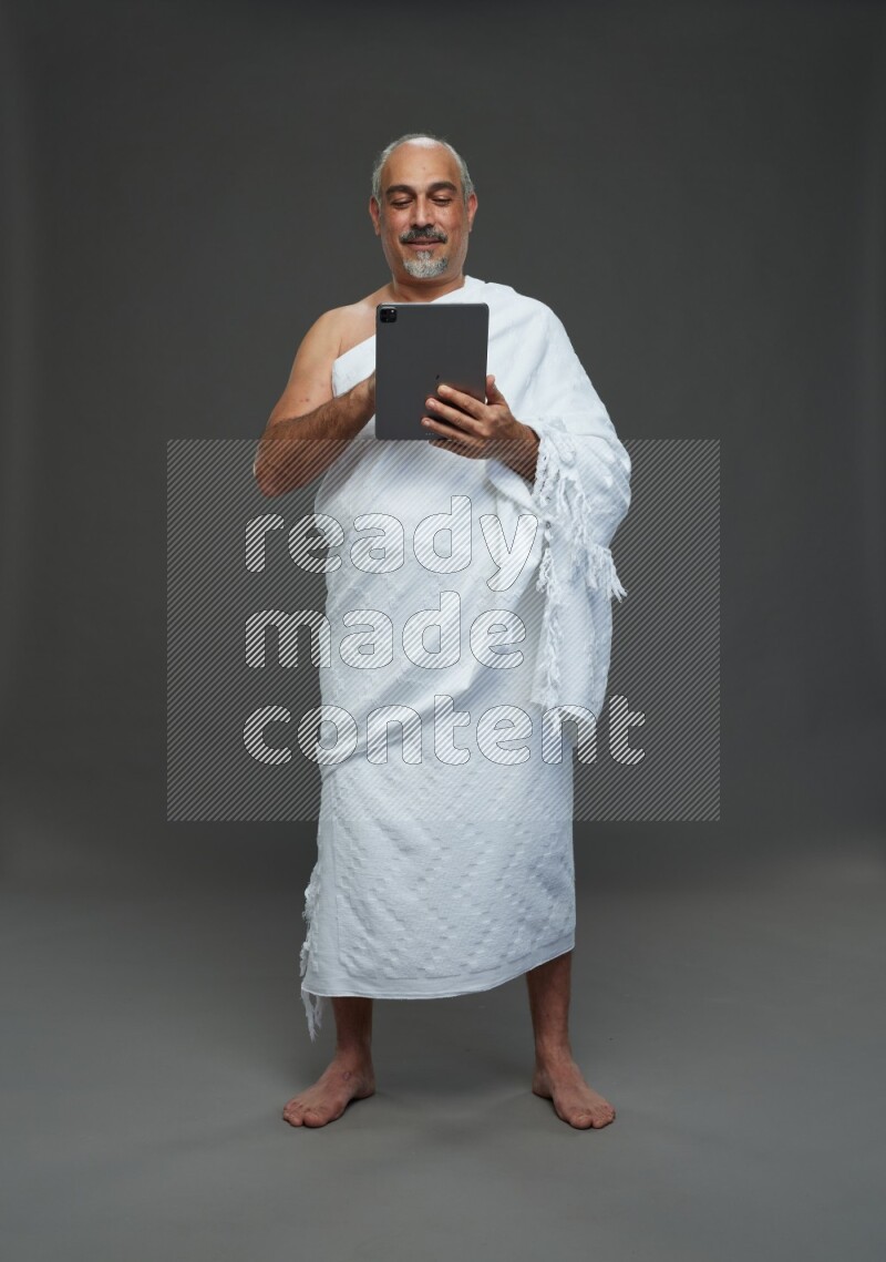 A man wearing Ehram Standing working on tablet on gray background