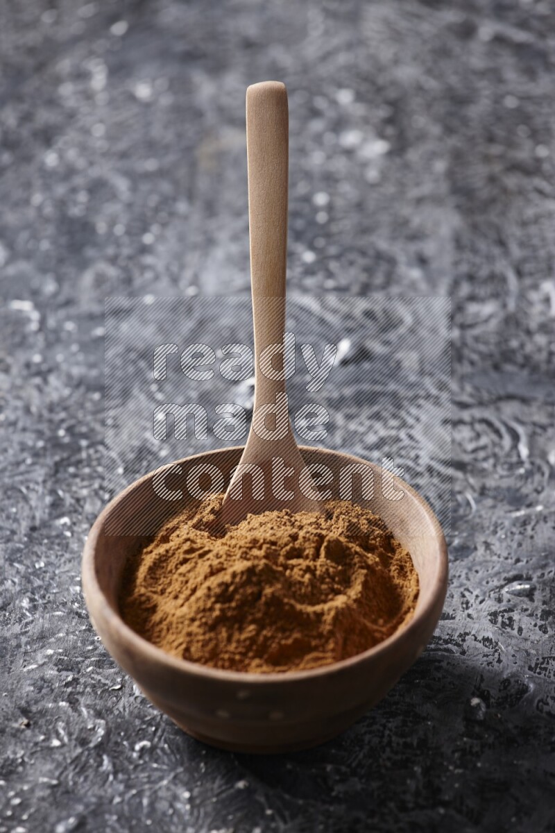 Wooden bowl full of cinnamon powder with a wooden spoon on a textured black background in different angles