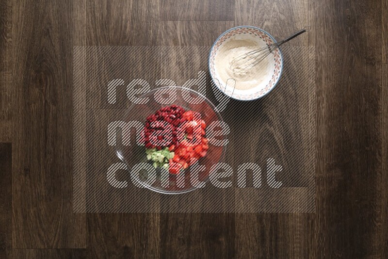 A bowl full of salad (avocado, tomatoes, red beans, olives, bell pepper, corn, lettuce) and bowl of salad dressing on wooden background