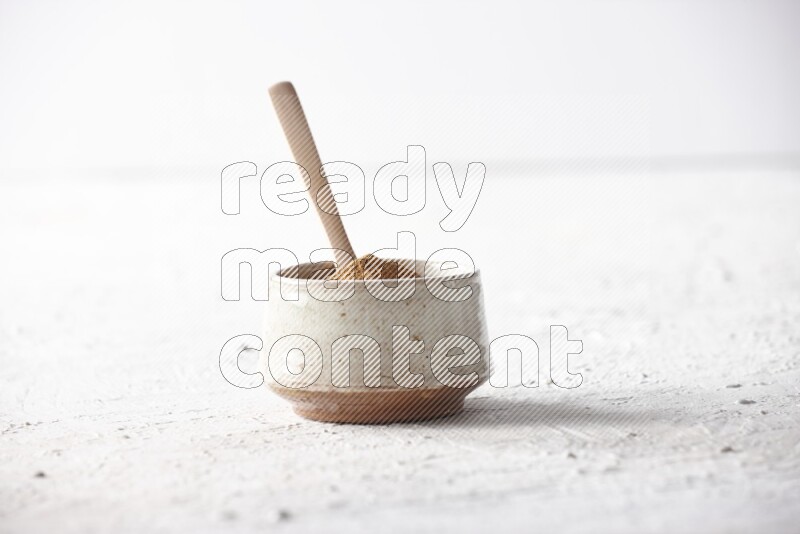 Ceramic beige bowl full of cinnamon powder with a wooden spoon on a textured white background