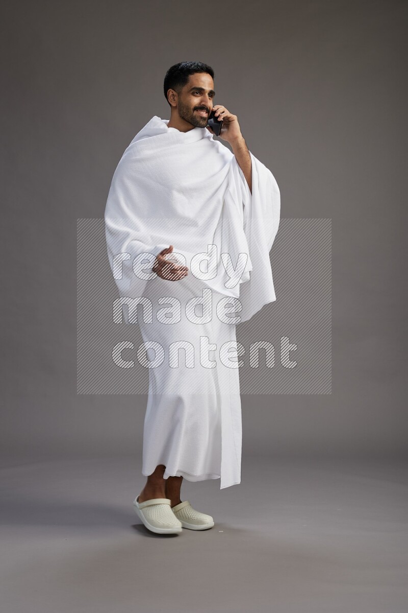 A man wearing Ehram Standing talking on phone on gray background