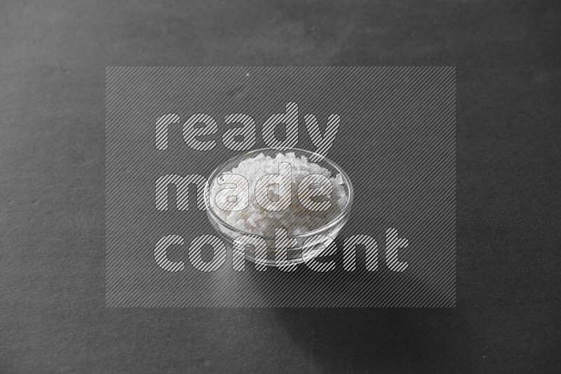 A glass bowl full of salt on black flooring