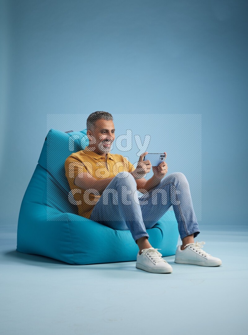 A man sitting on a blue beanbag and playing on phone