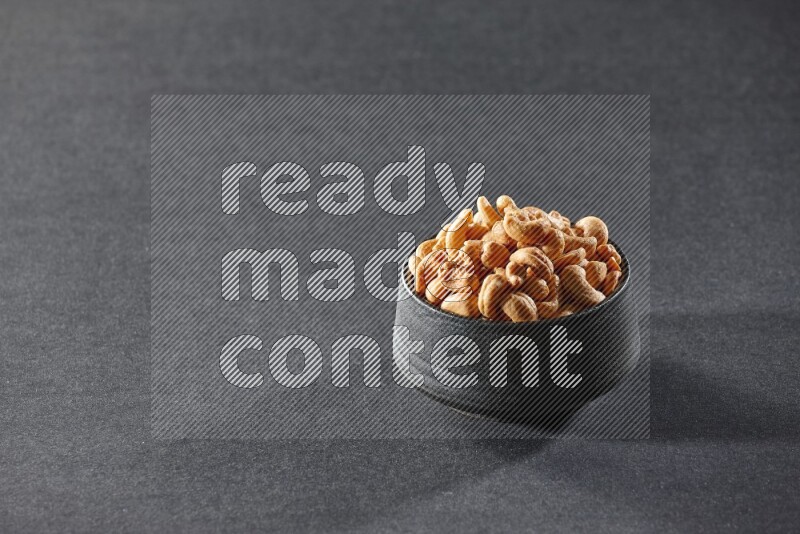 A black pottery bowl full of cashews on a black background in different angles
