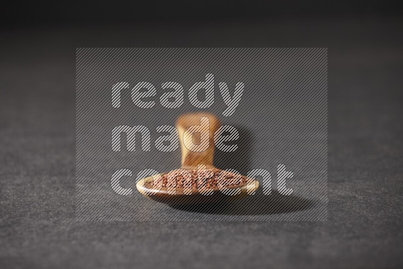 A wooden ladle full of garden cress seeds on a black flooring