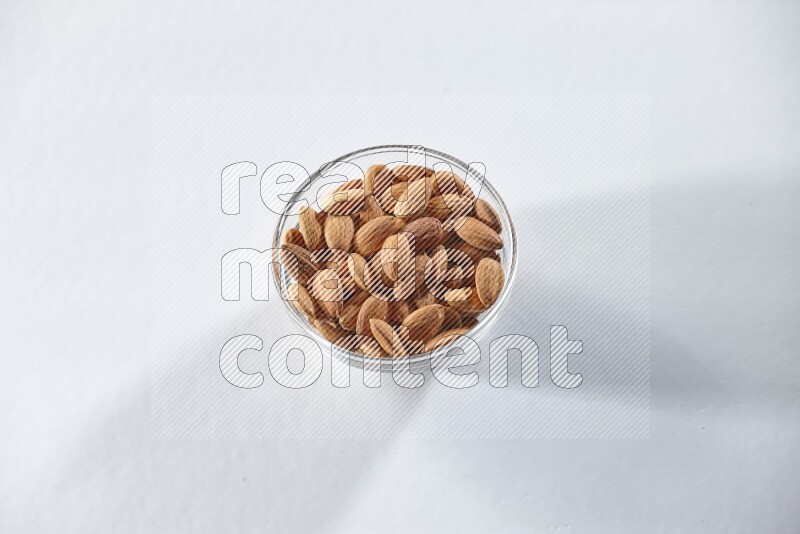 A glass bowl full of peeled almonds on a white background in different angles