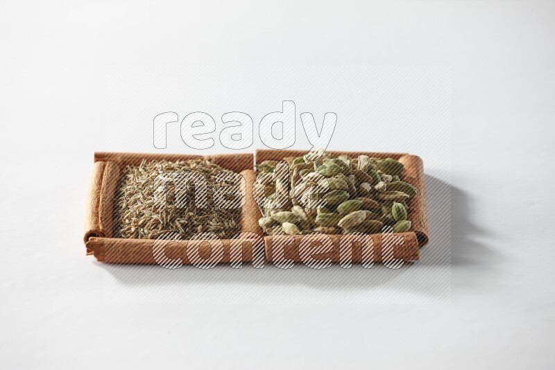 مربعان من أعواد القرفة ممتلئان بحبوب الهيل والكمون علي خلفية بيضاء