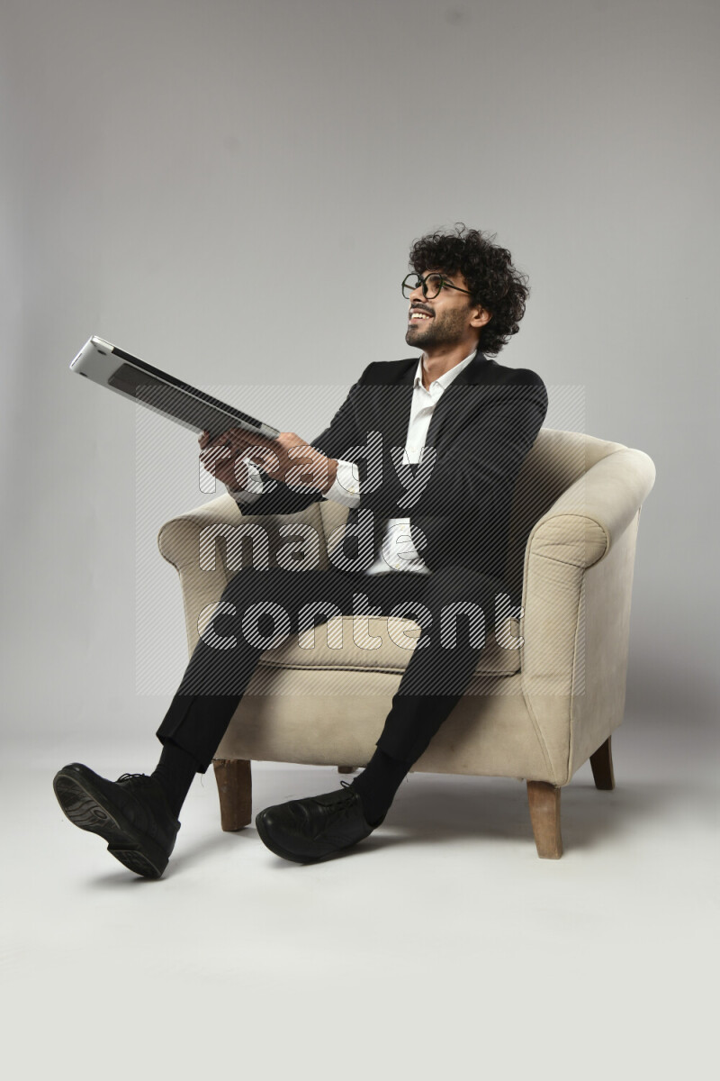 A man wearing formal sitting on a chair holding a laptop on white background