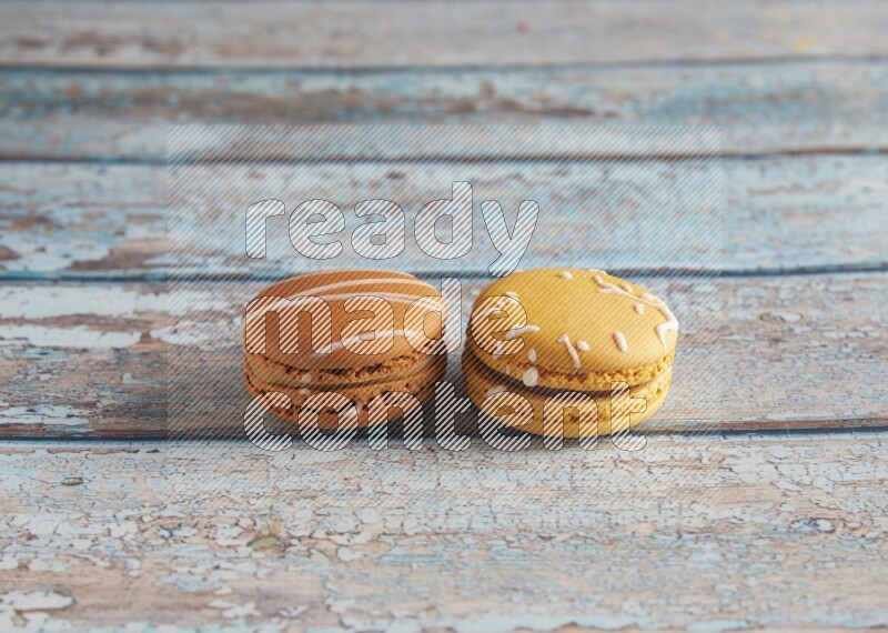 45º Shot of of two assorted Brown Irish Cream, and Yellow Piña Colada macarons on light blue background