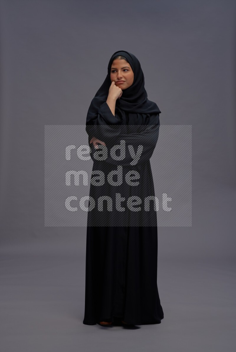 Saudi woman wearing Abaya standing interacting with the camera on gray background