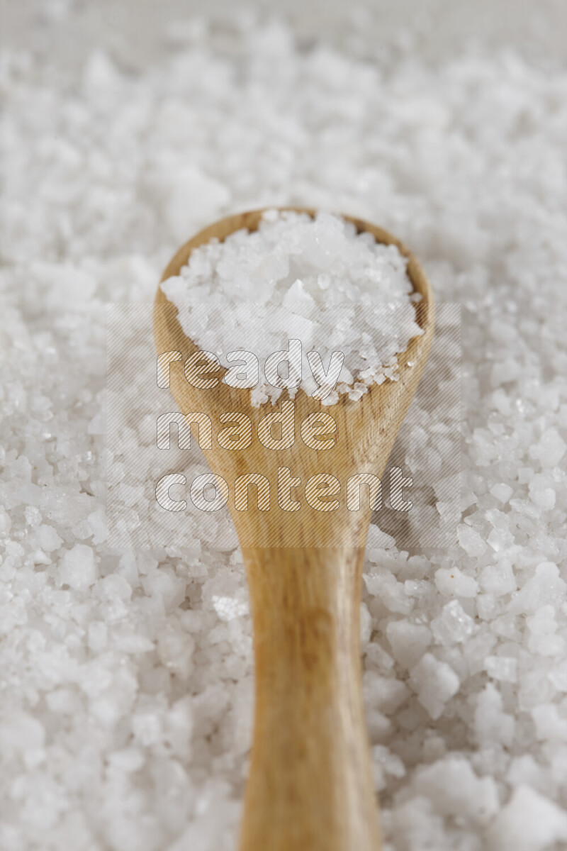 A wooden spoon full of white salt on white background