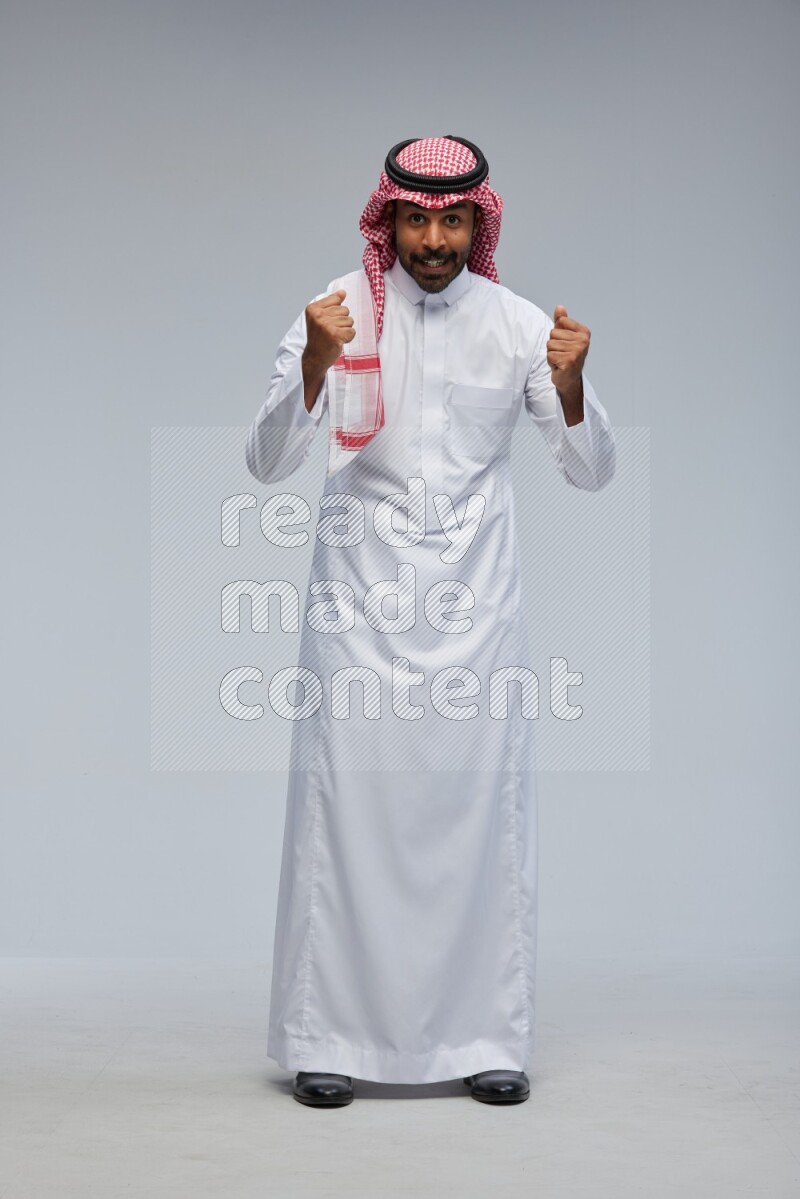 Saudi man Wearing Thob and shomag standing interacting with the camera on Gray background