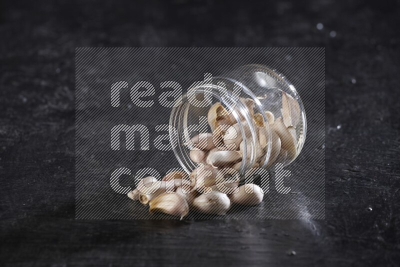 A glass jar full of garlic cloves flipped and the cloves came out on a textured black flooring