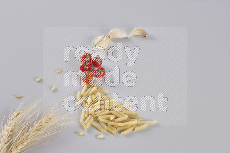 Mini penne with garlic, cherry tomatoes and wheat stalks on light grey background