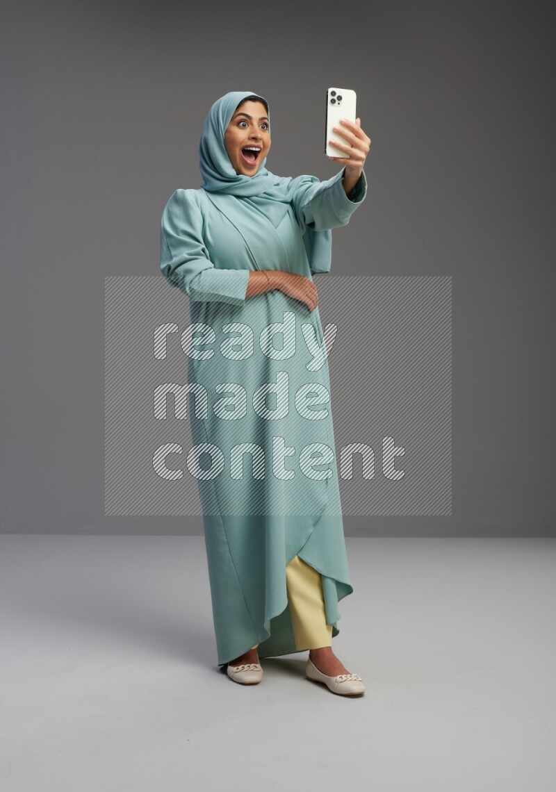Saudi Woman wearing Abaya standing taking selfie on Gray background