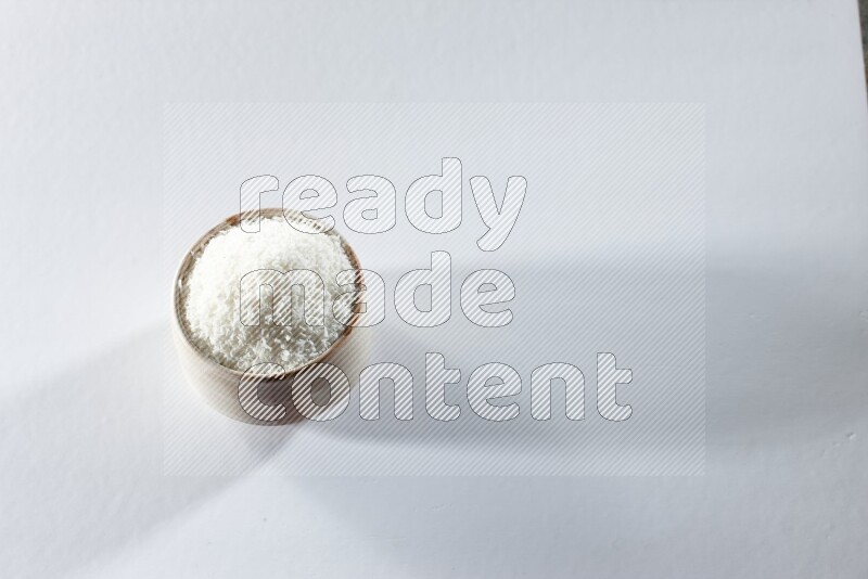 A beige ceramic bowl full of desiccated coconut on a white background in different angles