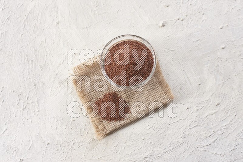 A glass bowl full of garden cress seeds on a burlap fabric on textured white flooring