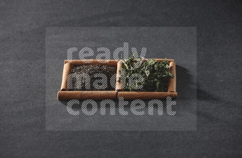 مربعان من أعواد القرفة ممتلئان بالشاي والنعناع المجفف علي خلفية سوداء