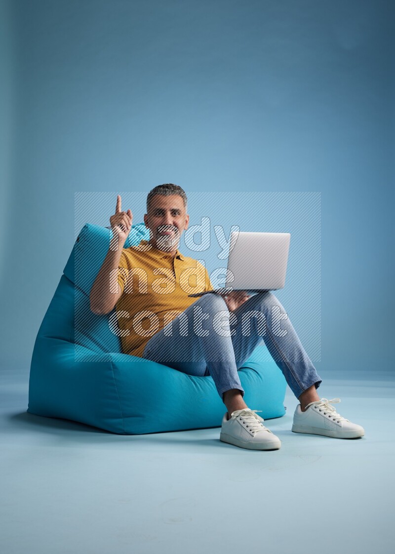 A man sitting on a blue beanbag and working on laptop