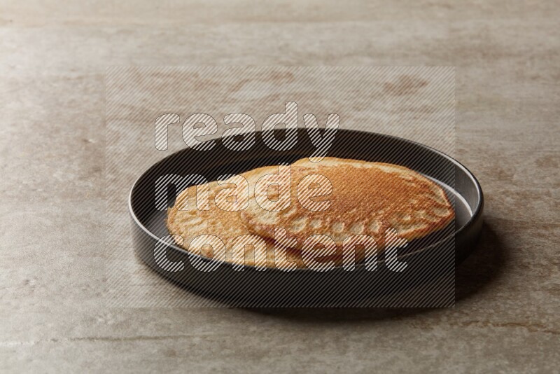Two stacked plain pancakes in a black plate on beige background