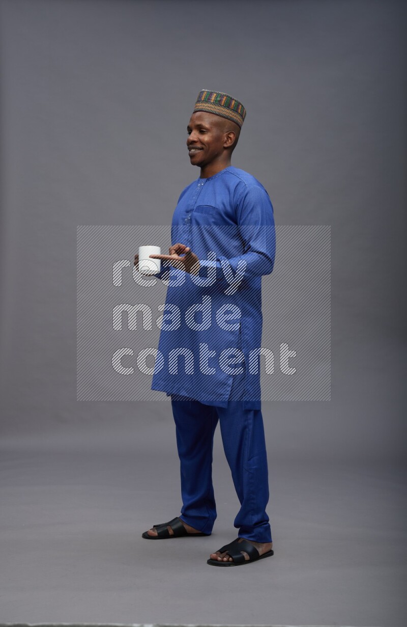 Man wearing Nigerian outfit standing holding mug on gray background