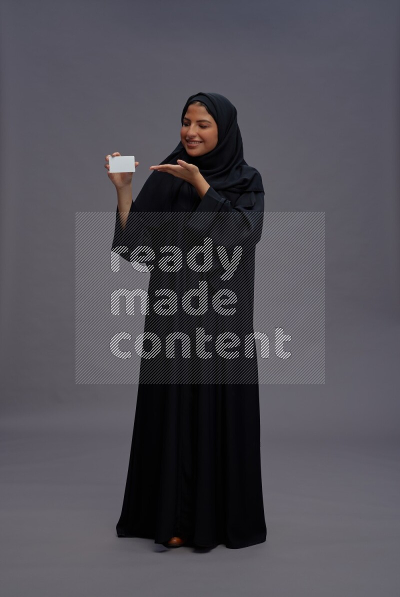 Saudi woman wearing Abaya standing holding ATM card on gray background