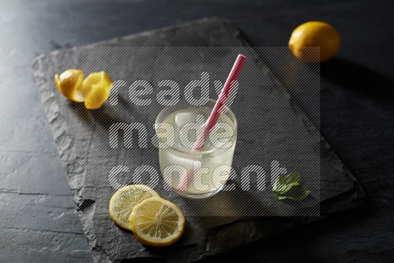 A glass of lemon juice with a straw on black background
