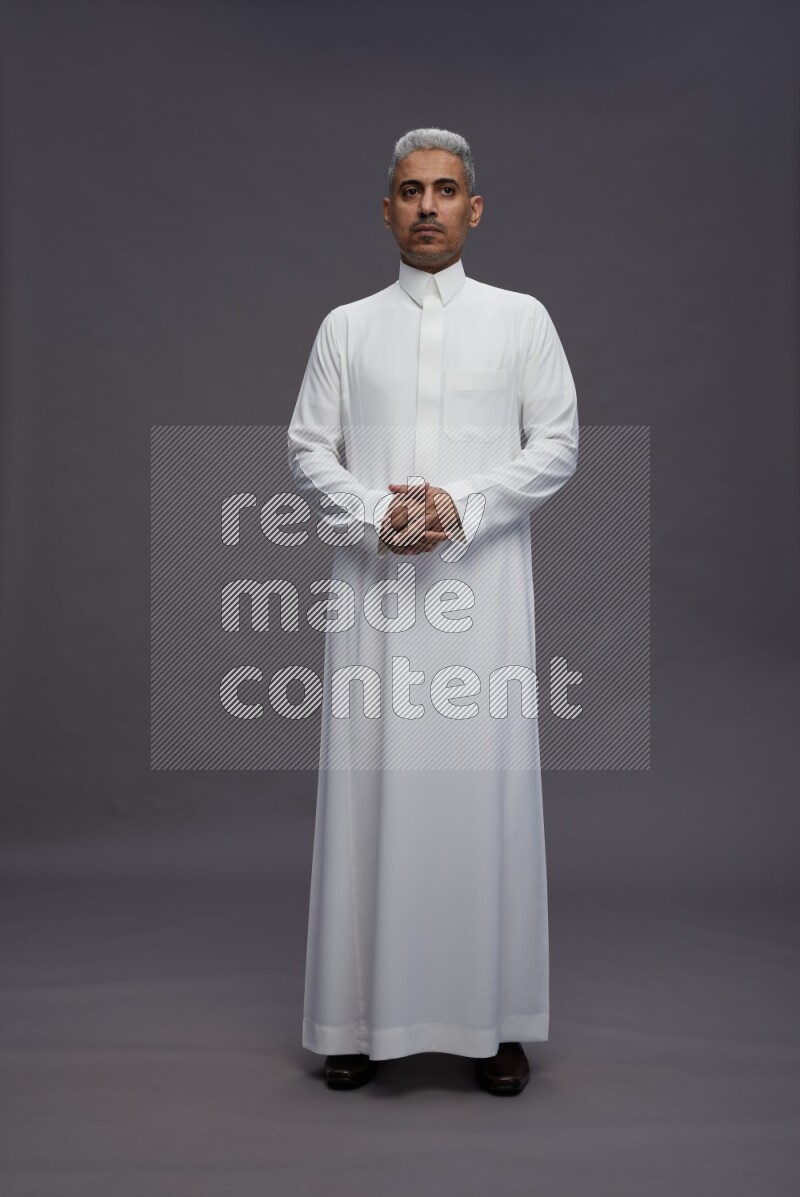Saudi man wearing thob standing interacting with the camera on gray background