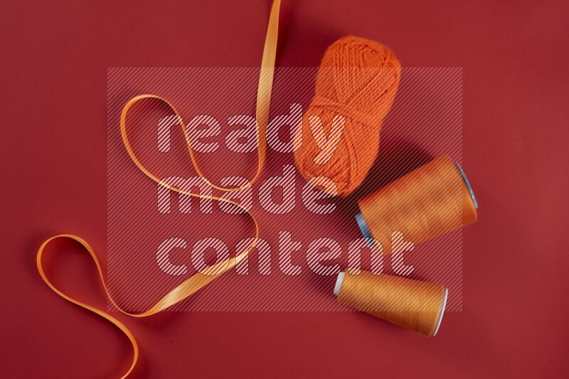 An orange collection of sewing and tailoring tools arranged on a red background