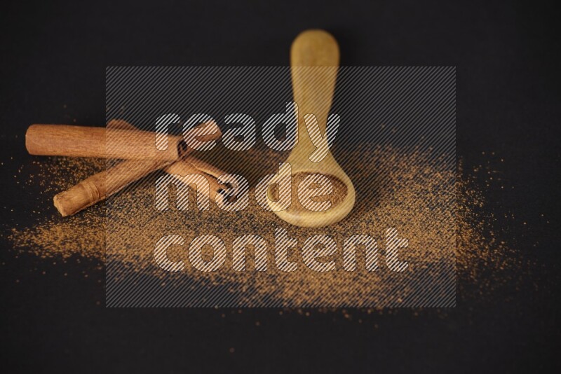 Cinnamon powder in a wooden spoon and cinnamon sticks beside it on black background