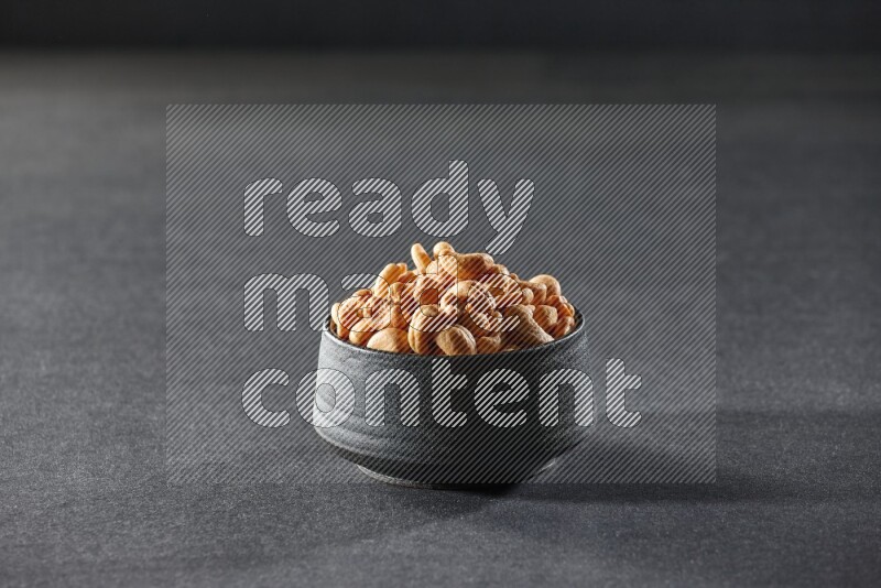 A black pottery bowl full of cashews on a black background in different angles