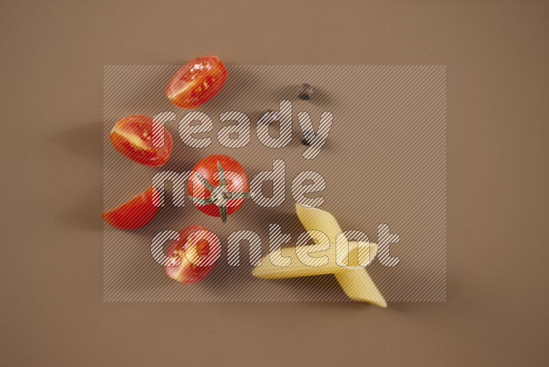 Raw pasta with different ingredients such as cherry tomatoes, garlic, onions, red chilis, black pepper, white pepper, bay laurel leaves, rosemary and cardamom on beige background
