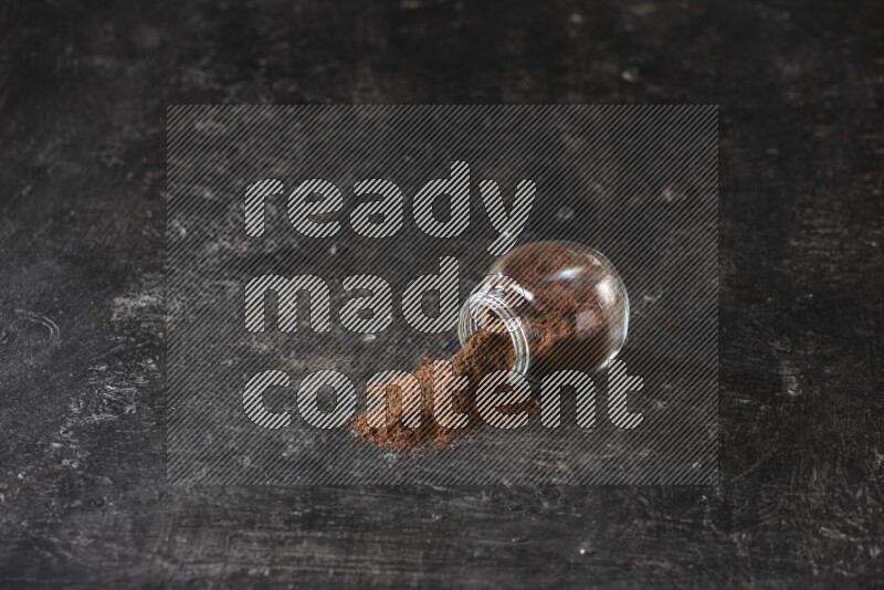 وعاء زجاجي للتوابل مقلوب ممتلئ ببودرة القرنفل والبودرة سقطت منه على أرضية سوداء