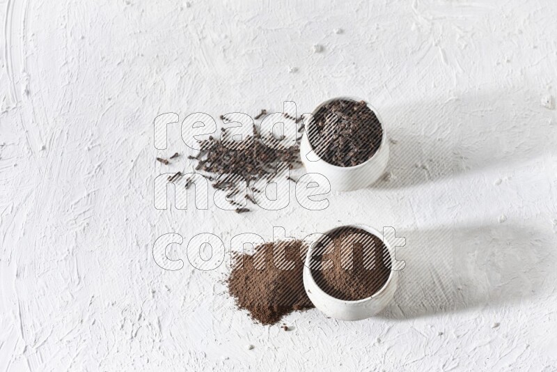 2 Beige ceramic bowls, one full of cloves and the other full of powder on textured white flooring