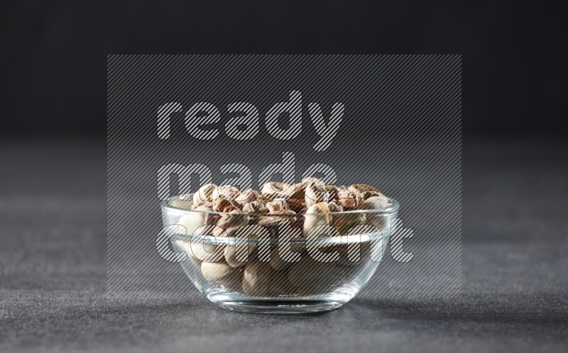 A glass bowl full of peeled pistachios on a black background in different angles