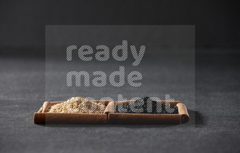 مربعان من أعواد القرفة ممتلئان ببذور السمسم وحبة البركة السوداء علي خلفية سوداء