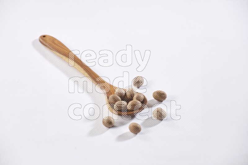 A wooden ladle full of whole nutmeg seeds on a white flooring