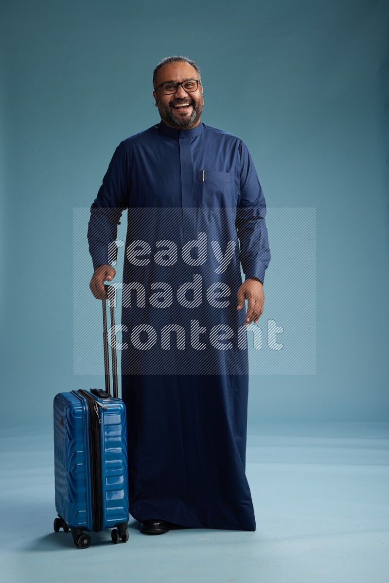Saudi Man without shimag Standing pulling travel bag on blue background