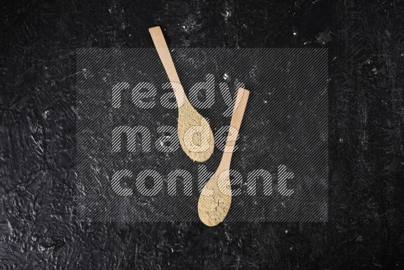 Two wooden spoons full of ground ginger powder on black background