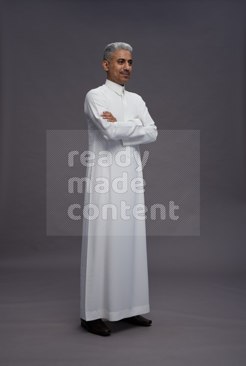 Saudi man wearing thob standing with crossed arms on gray background