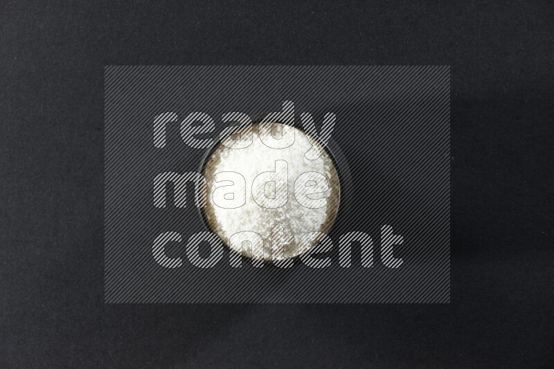 A black pottery bowl full of desiccated coconut on a black background in different angles
