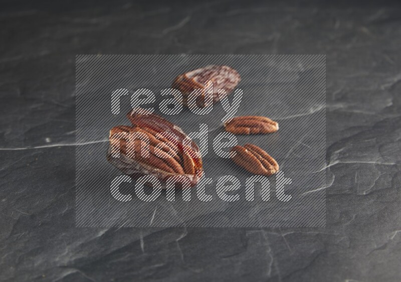 two pecan stuffed madjoul dates on a black textured background