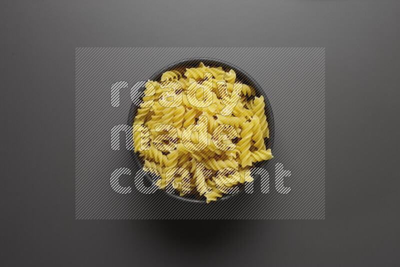 Fusilli pasta in a pottery bowl on grey background