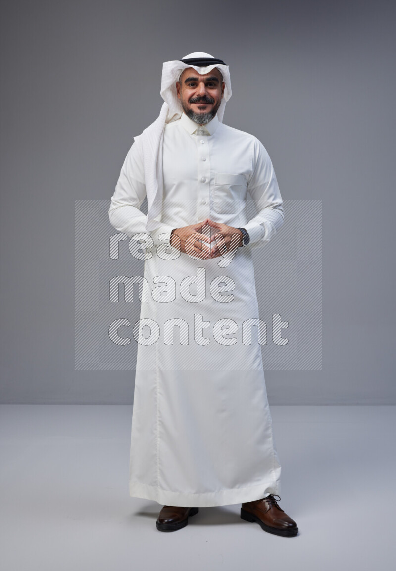 Saudi man Wearing Thob and white Shomag standing interacting with the camera on Gray background
