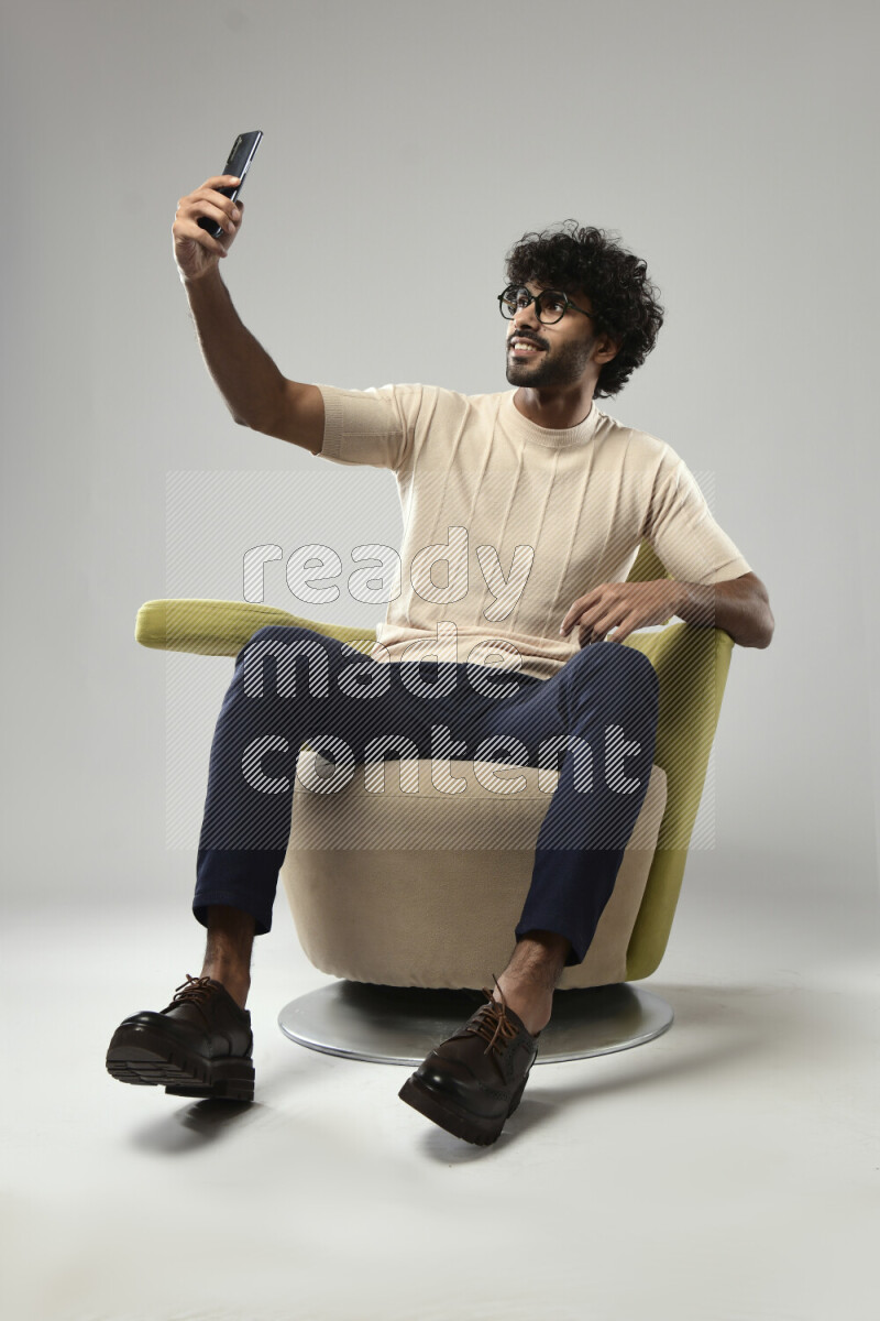 A man wearing casual sitting on a chair taking a selfie on white background