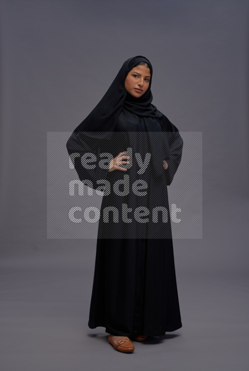 Saudi woman wearing Abaya standing interacting with the camera on gray background