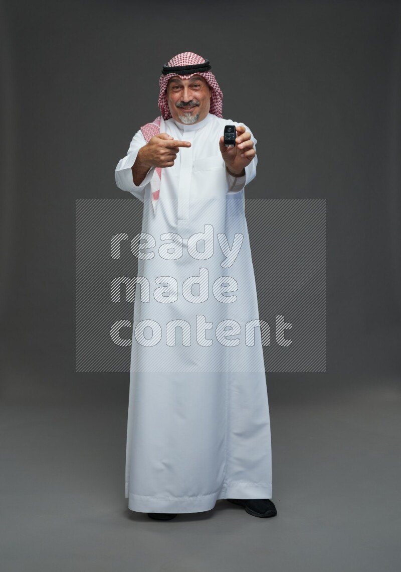 Saudi man with shomag Standing holding car key on gray background