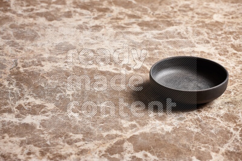 A black pottery bowl on beige marble background