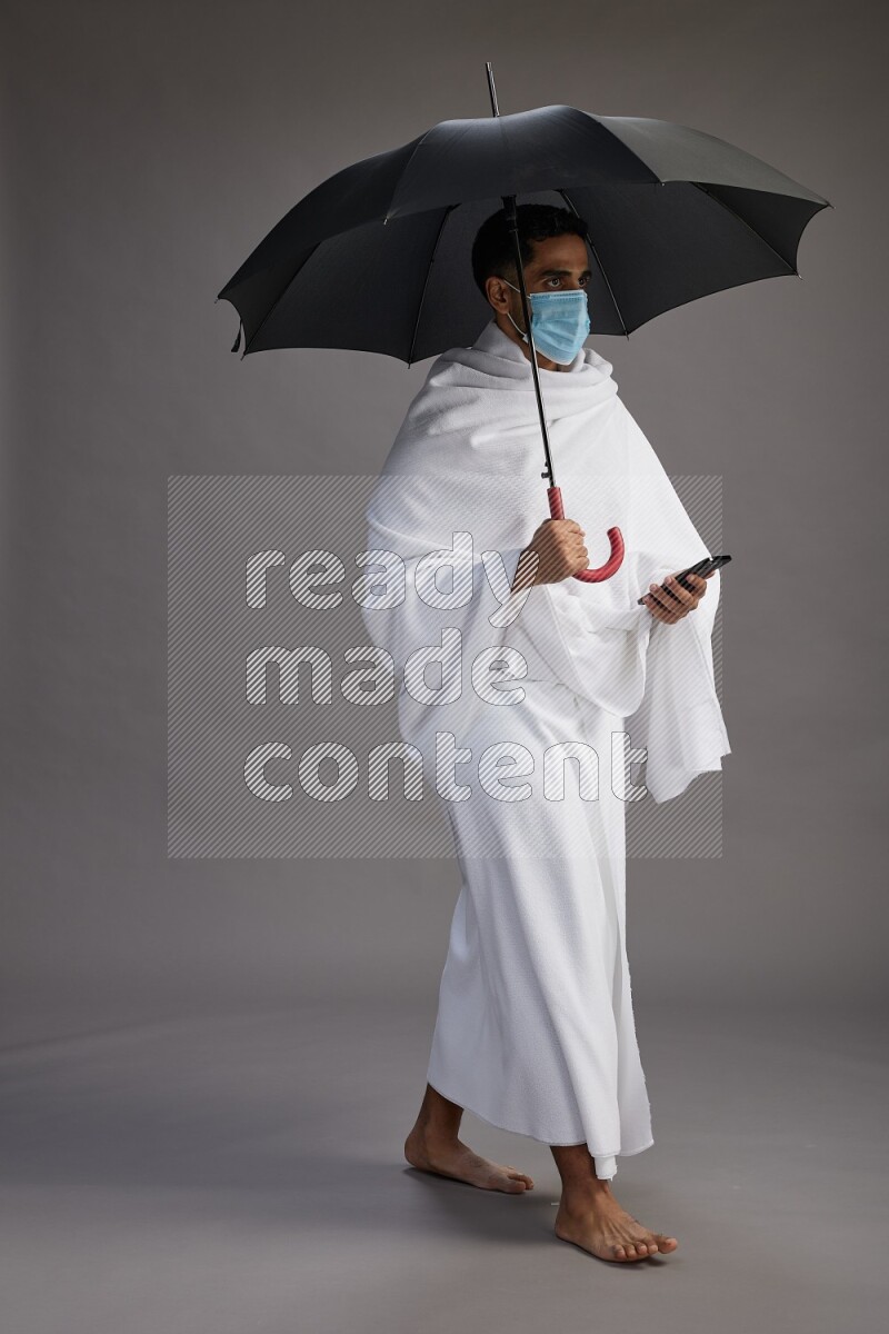 A man wearing Ehram and mask Standing holding umbrella on gray background on gray background