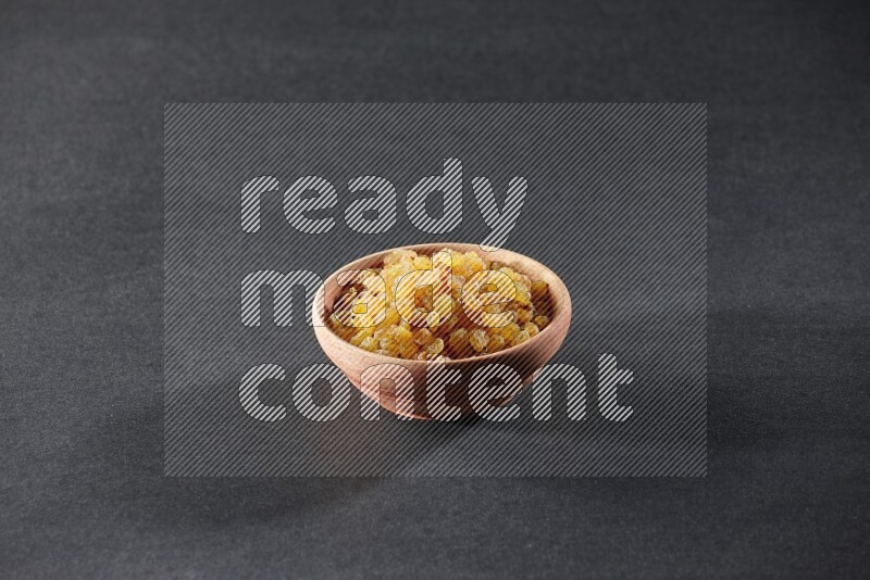 A wooden bowl full of raisins on a black background in different angles